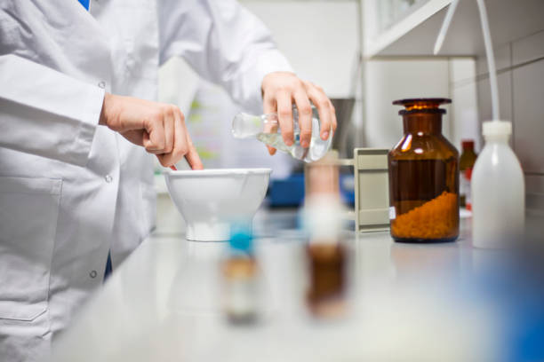 Female scientist making medicine in laboratory Midsection of female scientist making medicine in laboratory. Professional using mortar and pestle while pouring solution from flask. She is working at pharmacy. homeopathic medicine photos stock pictures, royalty-free photos & images