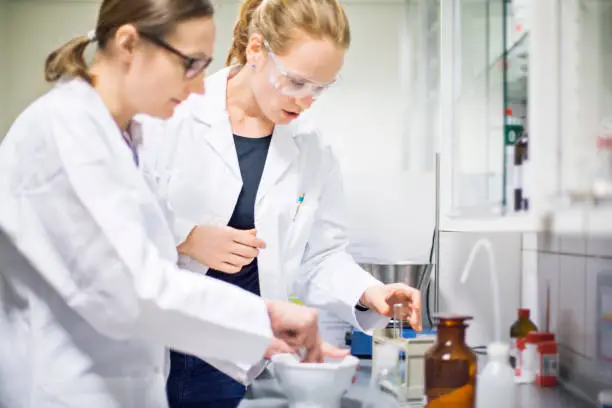 Female scientists making medicine at laboratory. Doctors are working together at pharmacy. They are wearing lab coats.