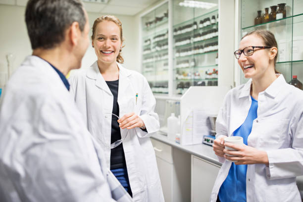 Happy scientists talking in laboratory at pharmacy Happy scientists talking in laboratory. Smiling male and female pharmacists are wearing lab coats. Professionals are at pharmacy. doctor utensils stock pictures, royalty-free photos & images