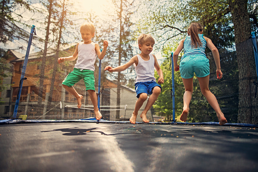 Little boys aged 5 and the girl aged 9 having fun jumping on trampoline. Sunny summer day
