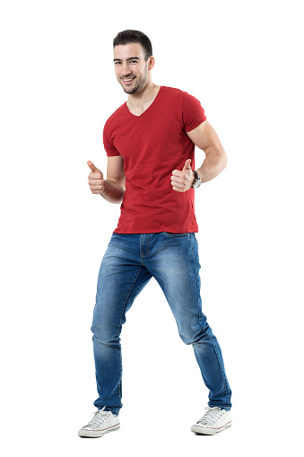 Cheerful excited young man in red t-shirt showing thumbs up gesture. Full body length portrait isolated over white studio background.