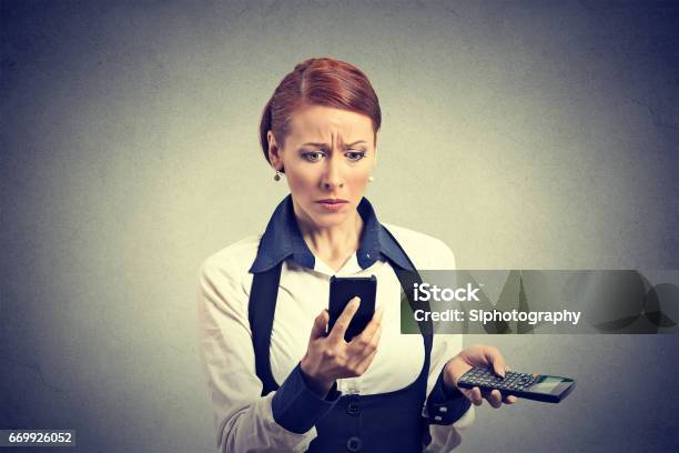 Sad Unhappy Upset Business Woman Looking At Smart Phone Holding Calculator Unexpected Financial Bills Charges Stock Photo - Download Image Now