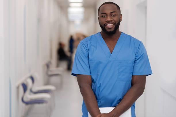 giovane afroamericano in piedi e sorridente in ospedale - nurse doctor healthcare and medicine african descent foto e immagini stock