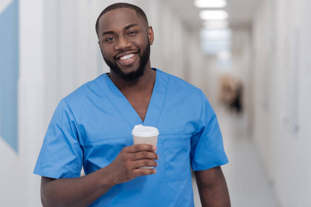 Happy African American intern enjoying coffee break in the clinic Taking pleasure in details. Friendly young African American intern standing in the hospital while enjoying coffee break and holding the cup of coffee anatomist photos stock pictures, royalty-free photos & images