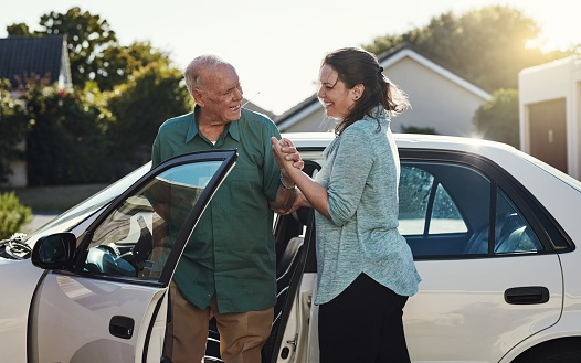 Shot of a woman helping her senior father out the car