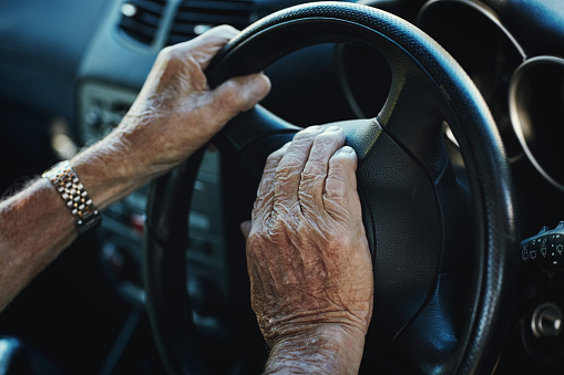 Closeup of a senior man's hands on the steering wheel of his car