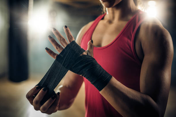 mulher de construção muscular irreconhecível envolvendo sua mão com uma bandagem antes do treino de boxe. - sports training muscular build women body care - fotografias e filmes do acervo