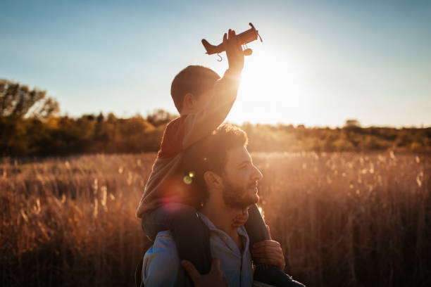 Playing with my dad outside Young father spending some quality outdoors time with his little boy, playing with an airplane model on shoulders stock pictures, royalty-free photos & images