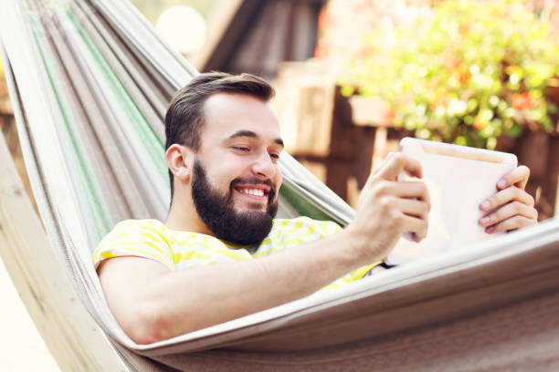 Picture showing happy man resting on hammock with tablet Picture of happy man resting on hammock with tablet hammock men lying down digital tablet stock pictures, royalty-free photos & images