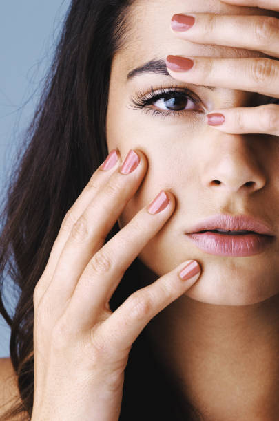 Studio shot of an attractive young woman touching her face to show off her beautiful nails against a gray background