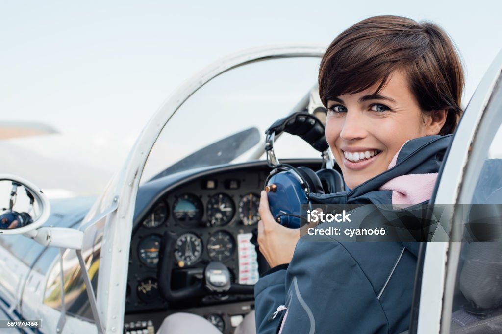 Pilot in the aircraft cockpit Smiling female pilot in the light aircraft cockpit, she is holding aviator headset and looking at camera Pilot Stock Photo