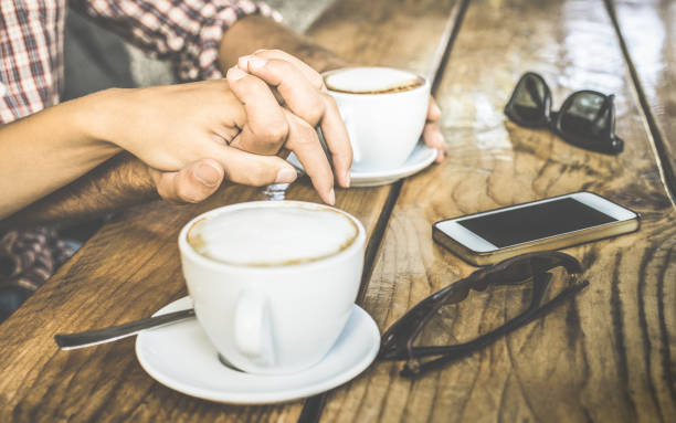 nahaufnahme von liebespaar trinken frischen cappuccino und spaß zusammen - jugend-beziehungskonzept mit jungen liebhabern zusammen an der kaffeebar - warm vintage retro-filter mit fokus auf händekreuz - coffee couple italy drinking stock-fotos und bilder