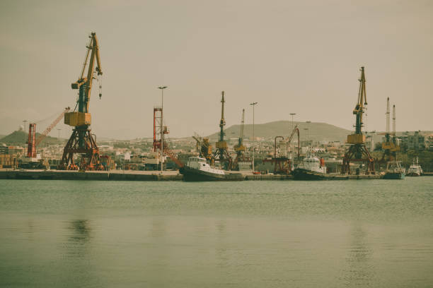 Harbor with industrial loading dock for ships in Heraklion, Crete, Greece with blue sky copy space, tug boats and a sailboat.