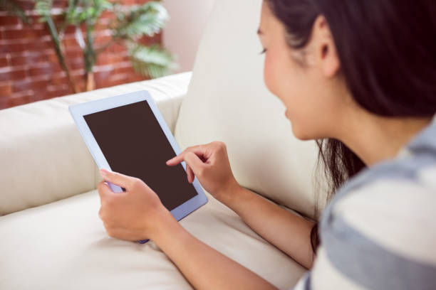 istock Smiling asian woman on couch using tablet 669985030