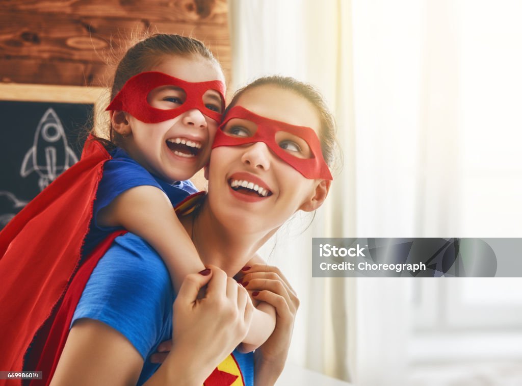 Girl and mom in Superhero costume Mother and her child playing together. Girl and mom in Superhero costume. Mum and kid having fun, smiling and hugging. Family holiday and togetherness. Mother Stock Photo