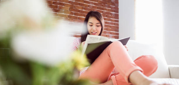 istock Smiling asian woman on couch reading 669988602