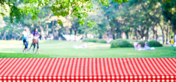 Empty table cover with red tablecloth over blur park with people background, for product display montage background, banner