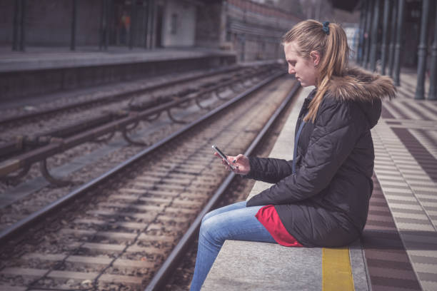 istock Young beautiful female using smartphone and sitting on train station platform 669990054