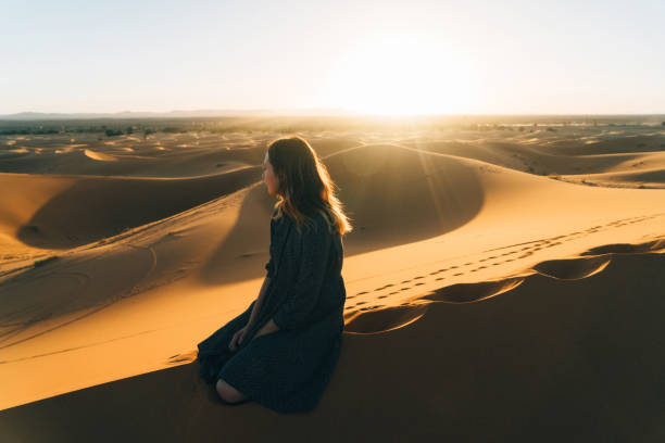 istock Woman sitting on sand in the desert 669992104