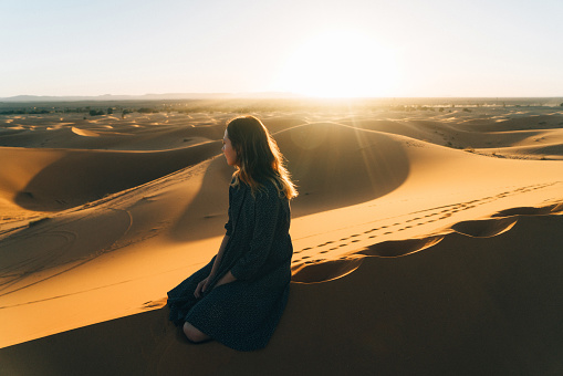 Young Caucasian woman sitting on sand  in the desert, Morocco