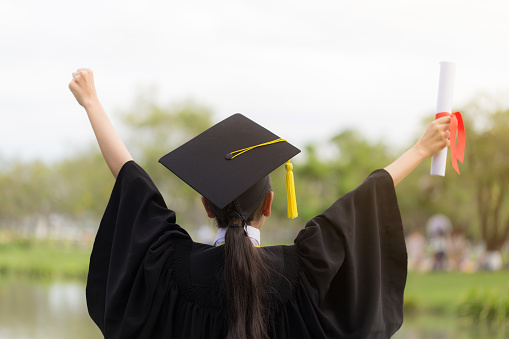 Graduate put her hands up and celebrating with certificate in her hand and feeling so happiness in Commencement day