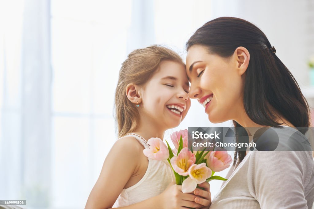 daughter congratulates mom Happy mother's day! Child daughter congratulates mom and gives her flowers tulips. Mum and girl smiling and hugging. Family holiday and togetherness. Mother Stock Photo