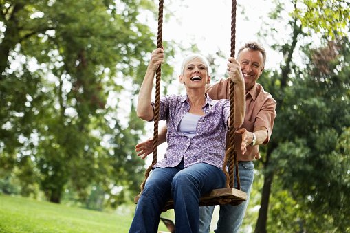 Mature couple on rope swing in park.