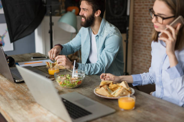 istock Two colleagues are eating food where they work on their laptops 670005022