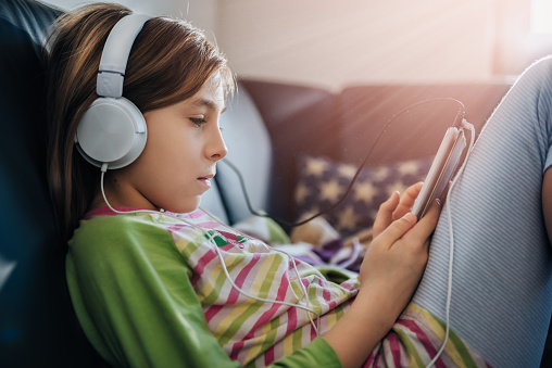 Girl sitting on black sofa using tablet and listening music