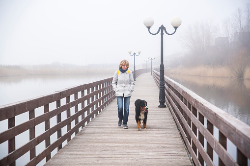 Mature attractive 50-years-old woman walking the dog on the boardwalk - approaching the camera. Kaliningrad, Russia, Baltic sea