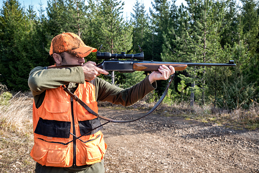 Portrait of a hunter in the forest aiming at his prey with a sniper rifle.