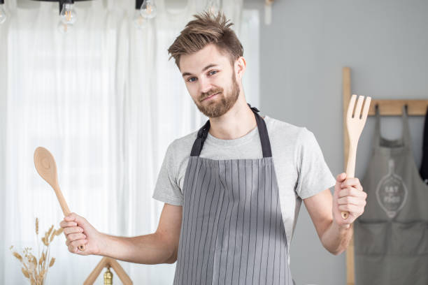 istock Young man cook showing wooden spoon fork in dining room 670018338