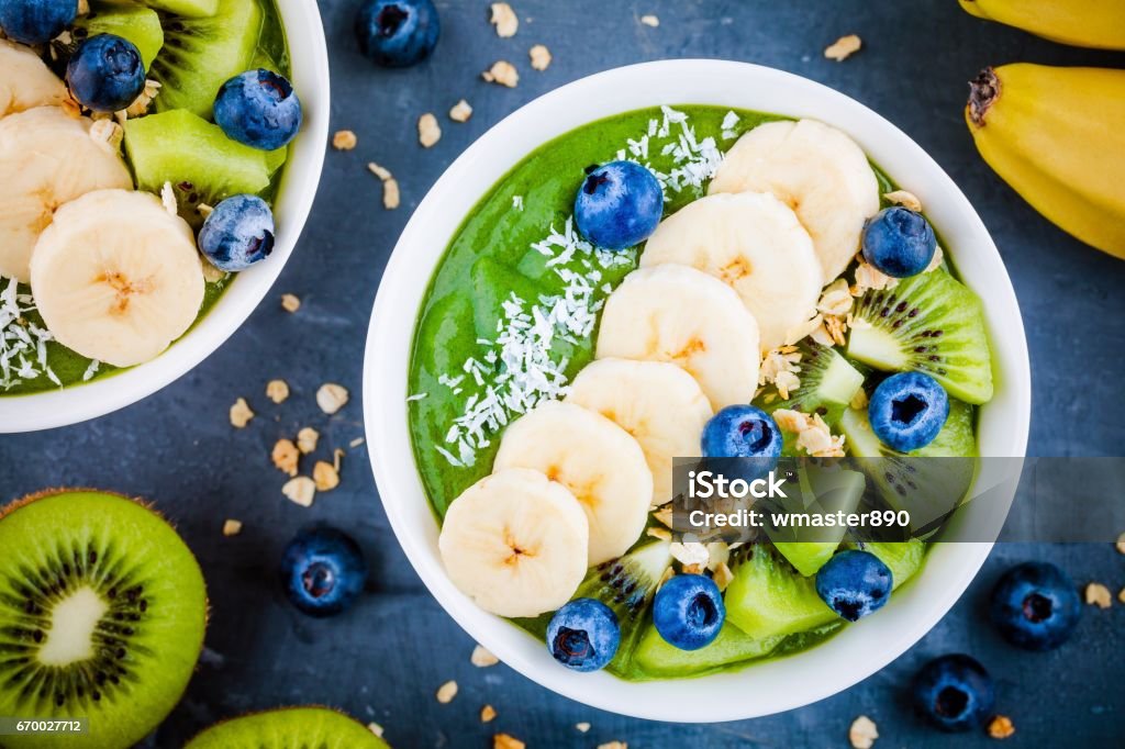 Tazón de fuente verde licuado con plátano, kiwi, arándano, granola - Foto de stock de Batido de frutas libre de derechos