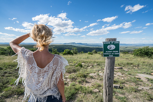 One young woman looking at the spectacular mountain scenery in Mountain Zebra national park in South Africa. Beware of lion warning sign beside the woman.