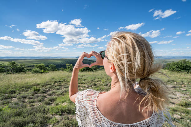 istock Young woman making heart shape frame on landscape 670032114