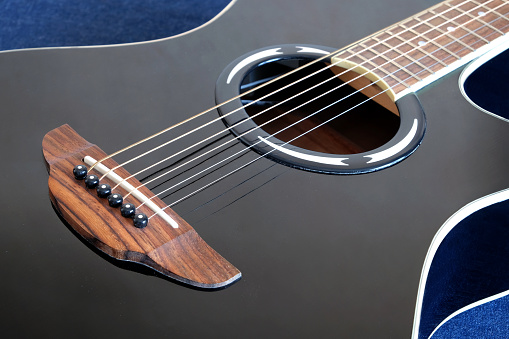 Classic acoustic six strings guitar black color top with cutaway fragment on jeans background side view closeup