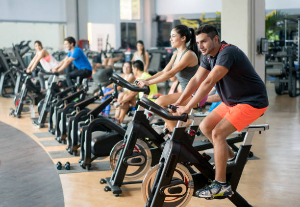 People exercising at the gym cycling Happy group of people training at the gym cycling on bikes - healthy lifestyle concepts spin bike stock pictures, royalty-free photos & images
