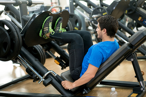 Healthy Latin American man exercising his legs at the gym on a leg press machine - fitness concepts