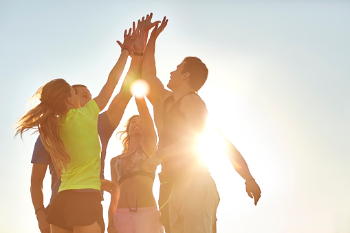 Low angle view of athletes high fiving after successful workout. Male and female friends are in sportswear. They are against clear sky on sunny day.