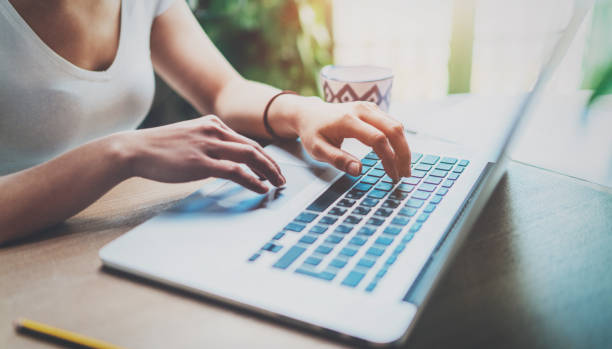 istock Young woman working at home on modern computer while sitting at the wooden table.Female hands typing on laptop keyboard.Concept of young modern people using mobile devices at home.Blurred background. 670055874