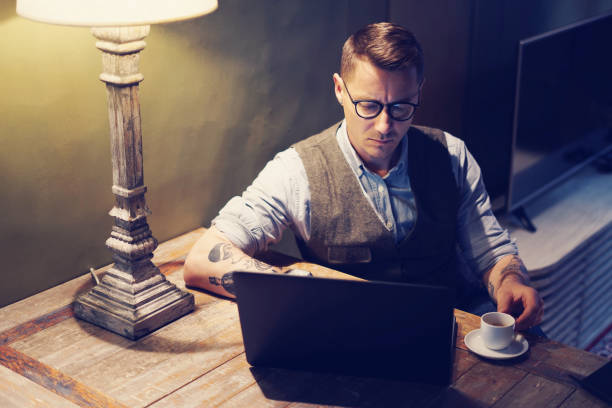istock Elegant tattooed man working at home on laptop while sitting at the wooden table.Using modern computer for research new startup ideas.Concept of business people work.Blurred background. 670060516