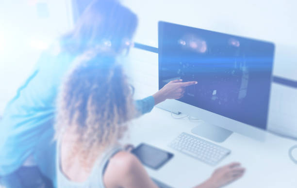istock Two young girl working on desktop computer in modern coworking studio.Coworkers using electronics gadgets.Icons,graphs and diagramm on monitor.Visual effect,color filter, blurred.Horizontal. 670075774