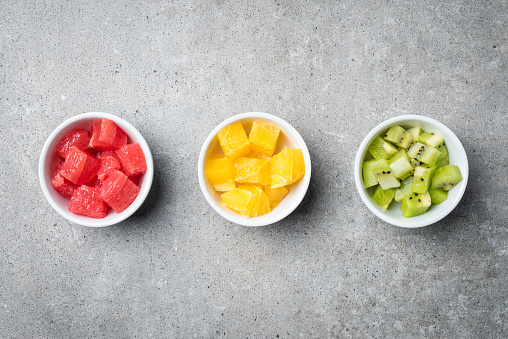 Overhead shot of cut fruits in white bowls on gray stone table