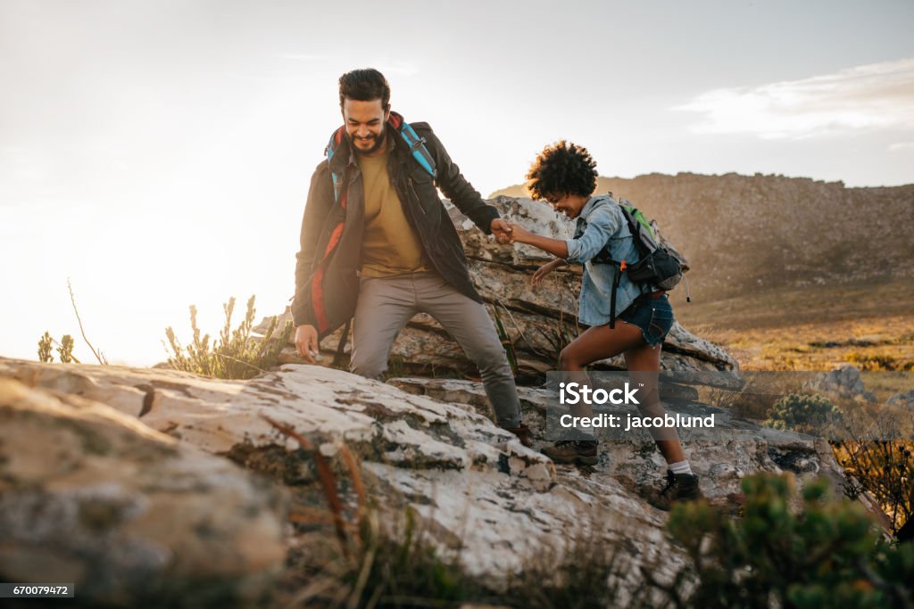 Young couple hiking in nature Young man helping friend to climb up the rock. Young couple hiking in nature. Hiking Stock Photo