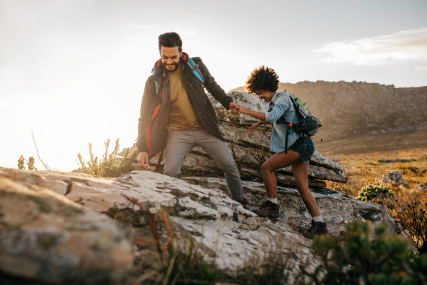 Young couple hiking in nature Young man helping friend to climb up the rock. Young couple hiking in nature. outdoor pursuit stock pictures, royalty-free photos & images