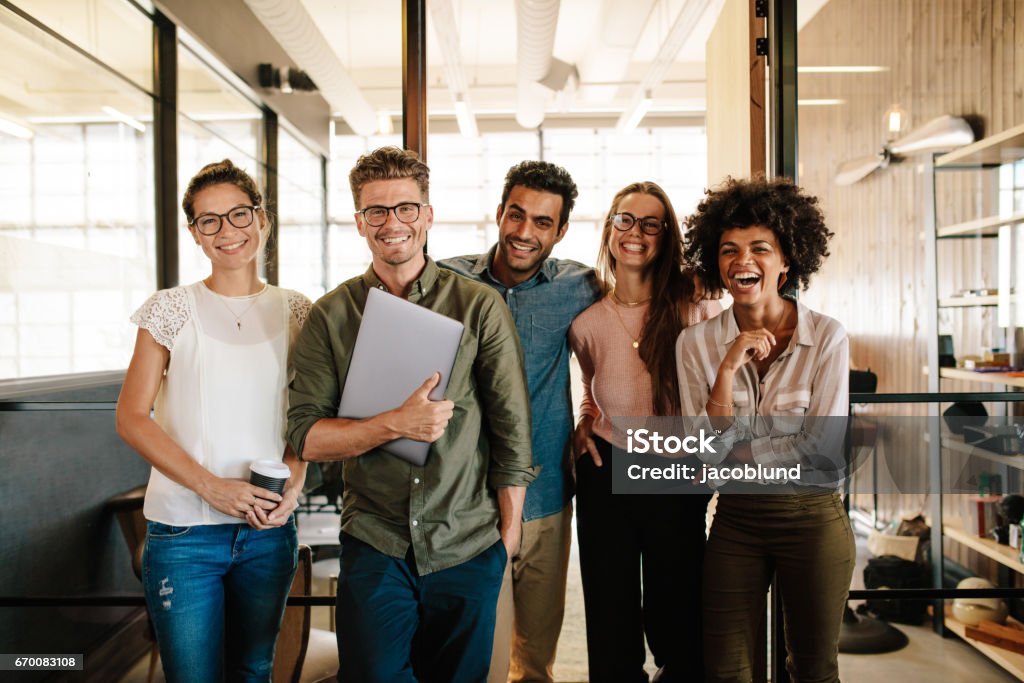 Creative business team laughing together Portrait of creative business team standing together and laughing. Multiracial business people together at startup. Teamwork Stock Photo