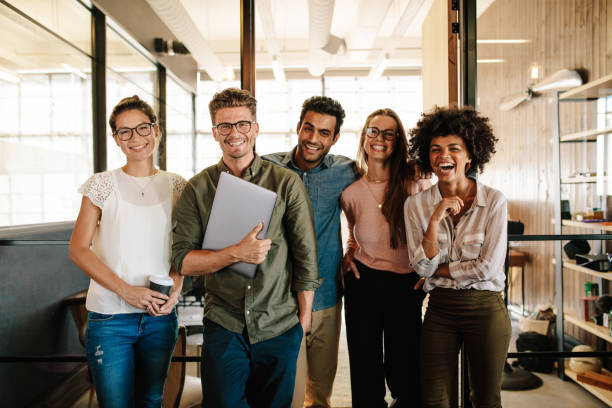 Creative business team laughing together Portrait of creative business team standing together and laughing. Multiracial business people together at startup. coworker stock pictures, royalty-free photos & images