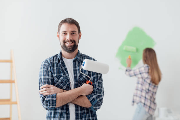 Home renovation and decor Home renovation, decoration and painting: man posing with paint roller, his girlfriend is working on the background house painter ladder paint men stock pictures, royalty-free photos & images