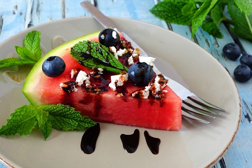 Slice of juicy watermelon pizza with blueberries, mint and feta cheese and balsamic glaze