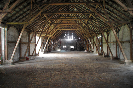 Empty rural barn with wooden supports and remains of hay on the floor